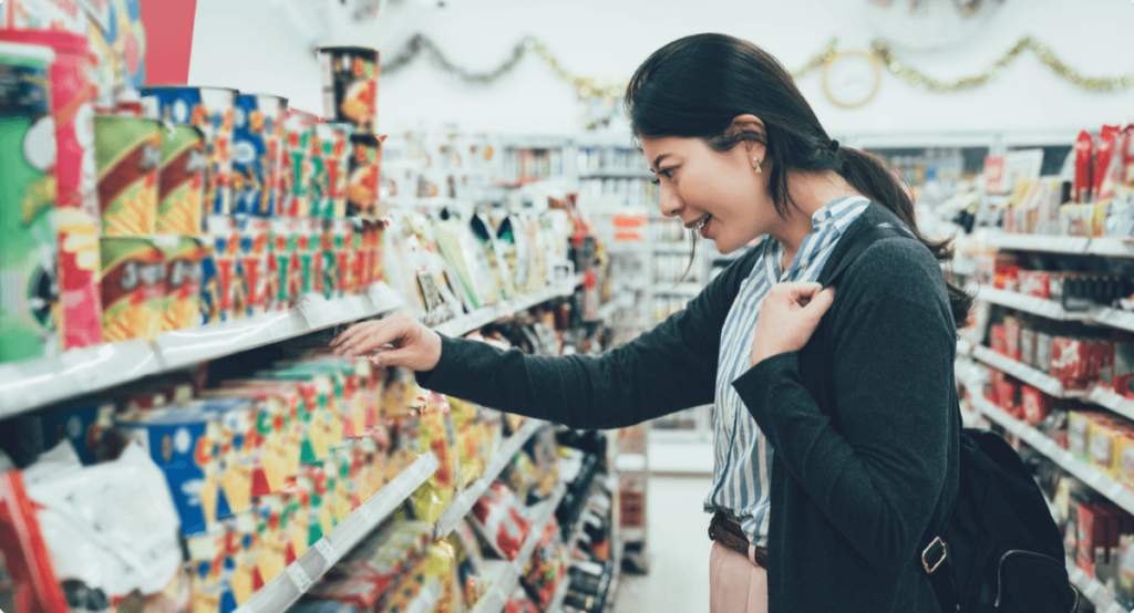 Woman shopping in convenience store, touching and looking at product in aisle while smiling.
