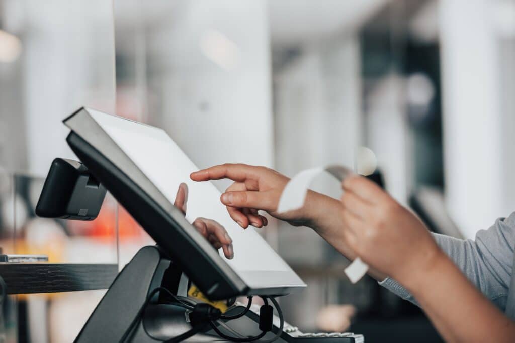 Two hands are shown. The left hand is hold a receipt, the right hand is about to press a button on a digital screen. Phygital retail is the merging of physical and digital experiences in the retail environment. 