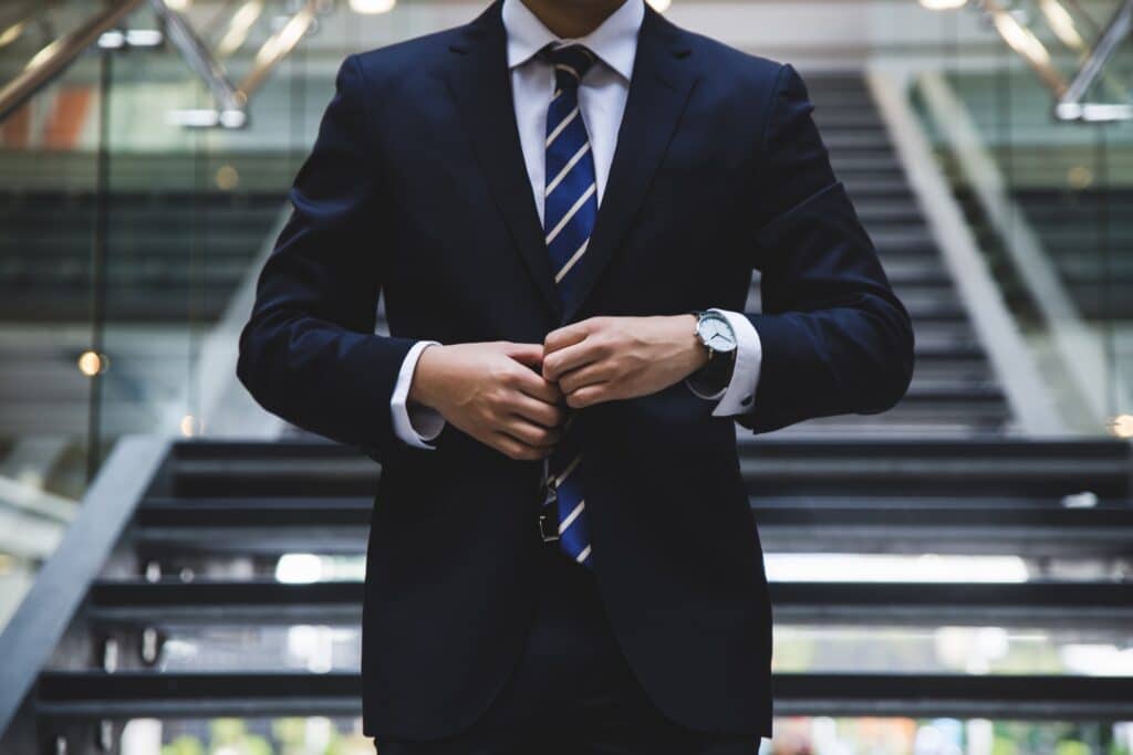 A man in a suit seen from the neck to the waist buttons up his jacket. Retail c-suite shake-ups may be able to be mitigated with better in-store testing. 