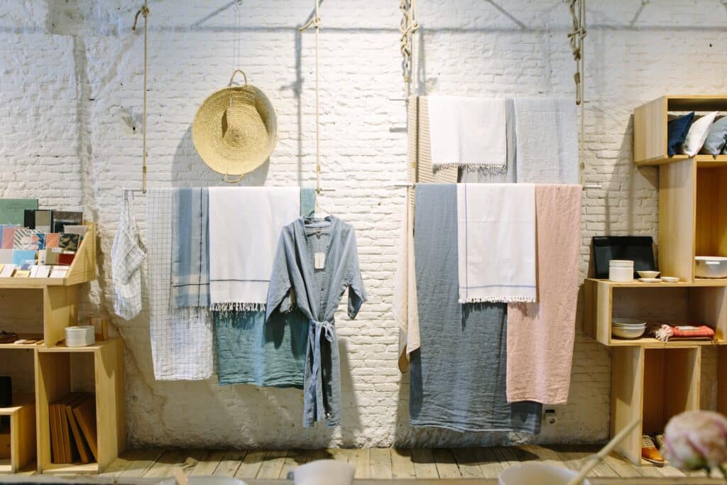 Fabrics, and a robe and woven basket hang by a string against a white brick wall. Pop-up shops are a creative way to attract attention to a brand.