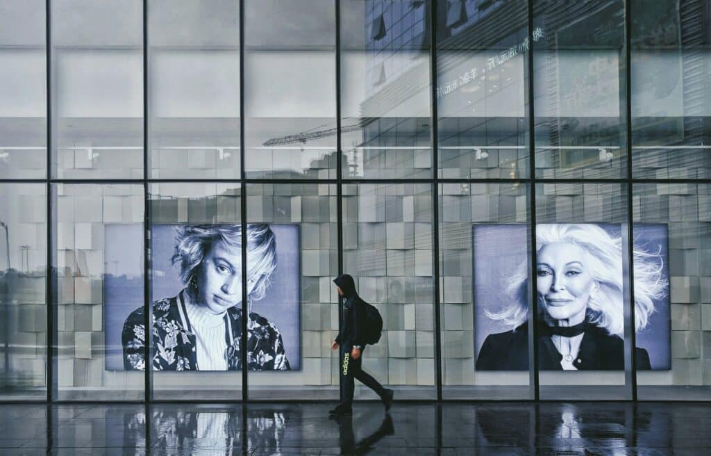 A person walks past a store window that has two large ads featuring women's faces in black and white. Using A/B testing and geo-tracking retailers gain insight into return on ad spend.